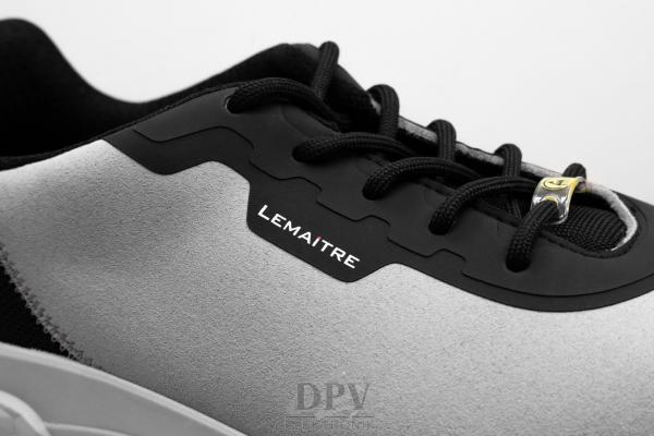 The image shows a close-up of a sports shoe. The shoe has a gray upper with black details and laces. On the side, there is the "Lemaitre" logo.