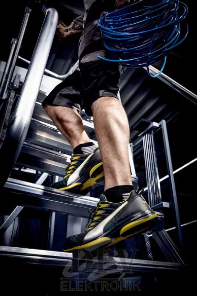 One leg is on a metal ladder rung. The wearer is sporting black and yellow athletic shoes. In their hand, they hold a cable that hangs down onto the steps.