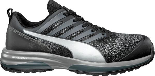 The shoe is sporty with a black upper and gray details. It has a flat sole, laces, and a textured, luminous area at the top.