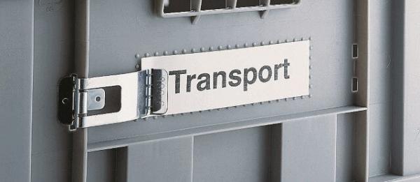 The image shows a gray transport box with a metallic clasp. On a plate, the word "Transport" is written in clear letters.