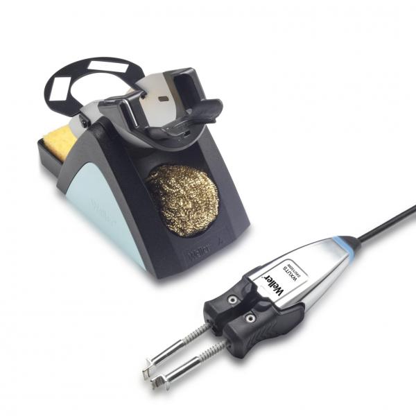 The image shows a soldering iron with a holder. The holder has a round opening and contains a brass cleaning spiral. A pressure device is attached to the cable of the iron.