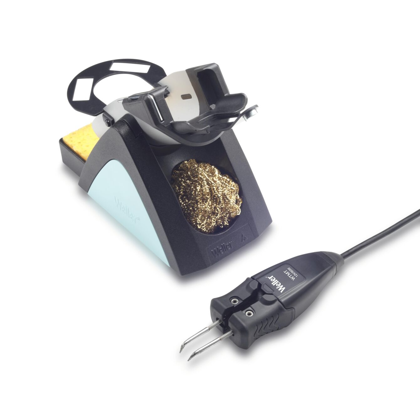 The image shows a soldering iron stand with a gold-colored soldering aid and a sponge. The soldering iron has a black grip surface and a plugged-in connection.