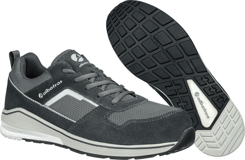 The image shows a gray athletic shoe made of textile and suede. It has a non-slip rubber sole with deep tread. The toe of the shoe is rounded, and the colors are predominantly dark gray.