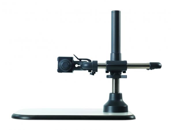 The image shows a device on a stable, flat table. It has a vertical cylinder, with a movable arm attached, and a camera mounted on the side. Everything is in black.