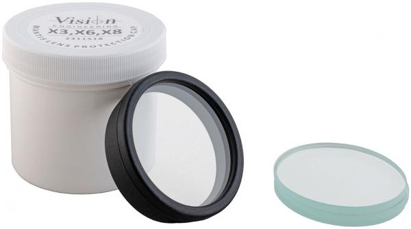 The image shows a white container with a screw top. Next to the container, there are two lenses: a clear lens with a black rim and a flat, green lens.