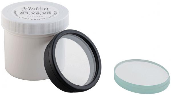 The image shows a round, black lens lying in a white container. Next to it is a flat, transparent lens in a light shade.