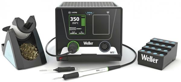 The image shows a soldering station with a digital display and temperature control, a soldering iron in a holder, a cleaning brush, and four soldering tips beside it.