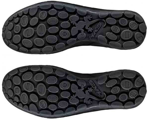 The image displays the undersides of two black shoe soles. They feature a textured surface with numerous round and oval protrusions to enhance grip.