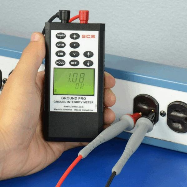 A handheld device for measuring soil conductivity, with a digital display showing a value of 1.08 ohms. It is connected to an outlet with two cables.