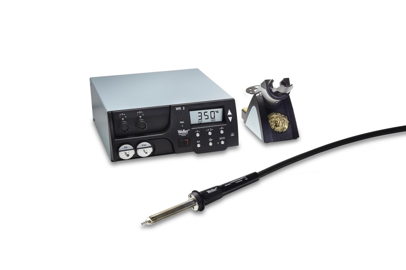 The image displays a soldering device with a digital temperature display. Next to the device, there is a soldering iron with a long cable and a soldering station. The predominant colors are grey and black.