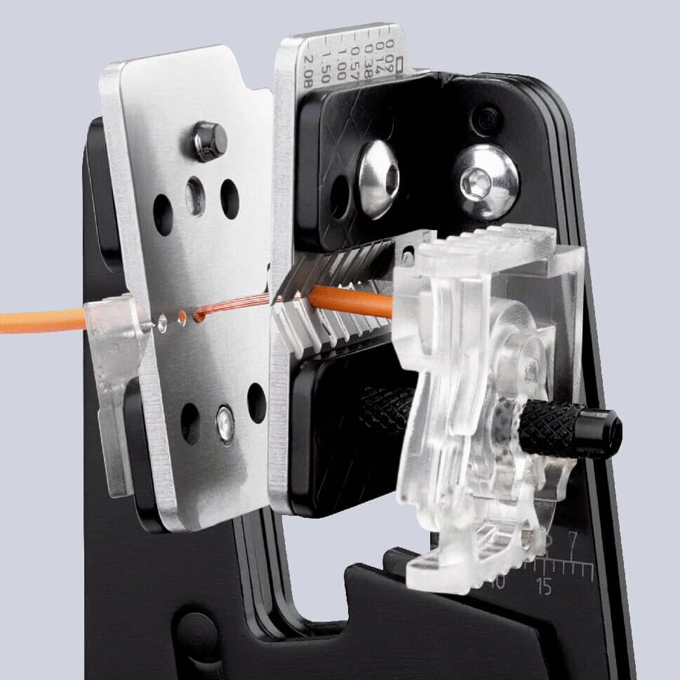 The image shows a crimping tool holding an orange wire in a holder. The tool has metallic parts with holes and a transparent plastic component for guiding the wire.