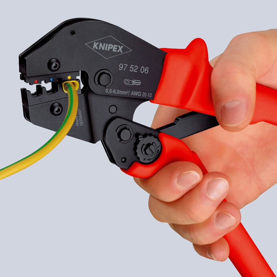 The image shows a hand holding a pair of wire cutters. The pliers have red handles and a black cutting surface, into which a green and yellow cable is inserted.