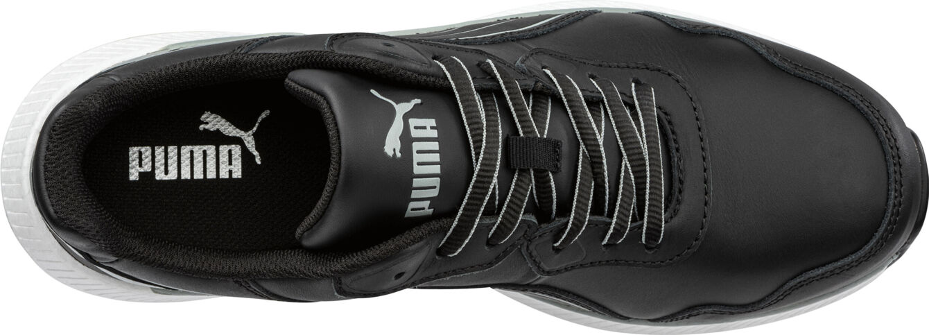 The image shows a black sports shoe from Puma. It has a smooth, leather-like surface, white shoelaces, and a white sole. The logo is subtly placed.