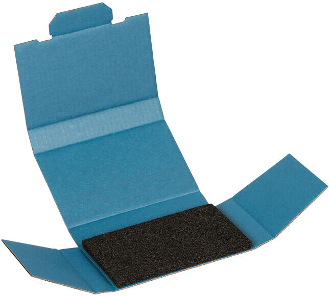 The image shows a blue package that is open. In the center lies a black, rectangular piece, possibly sandpaper or a similar material. The packaging has folded surfaces.