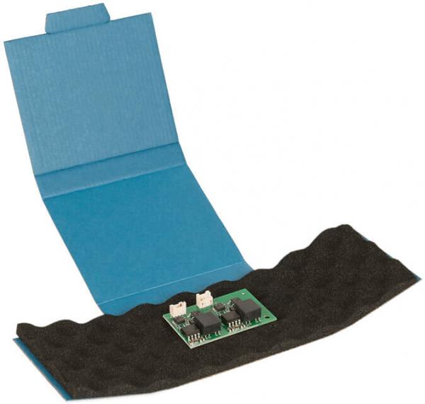 The image shows an open, blue package with a soft black lining. On it lies a green circuit board with two small components.