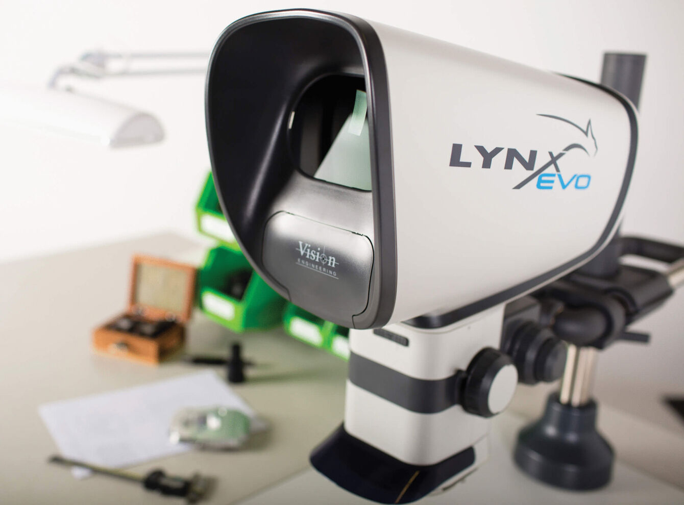 The image shows a device called LYNX Evo, which looks like a small telescope. It has a black opening at the front, a gray and white casing, and is mounted on a stable gray base.