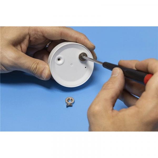 A hand is holding a screwdriver, currently turning a screw into a round white component. Next to it, a small metal washer lies on a blue surface.