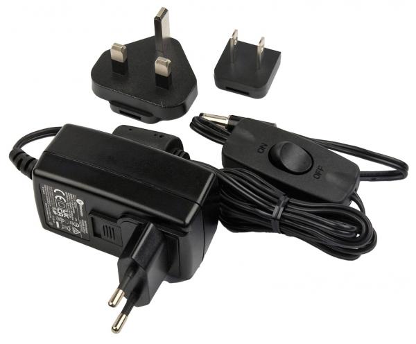 The image displays a black power supply with a cable and a switch. Next to the power supply, there are two different plugs, one with two round pins and one with two flat ones.