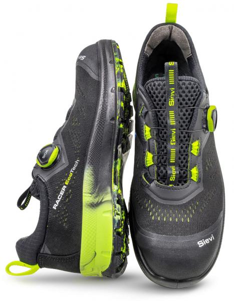 The image shows a pair of high-quality sports shoes. They are primarily black with bright yellow accents. The lacing has been replaced by a streamlined system, and the soles provide grip.