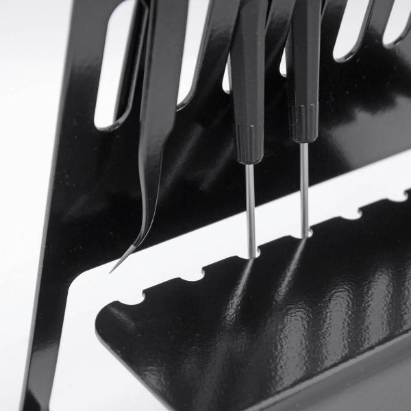 The image shows a black holder with various tools. Three long, thin tools protrude, with differently shaped tips. The background is light.