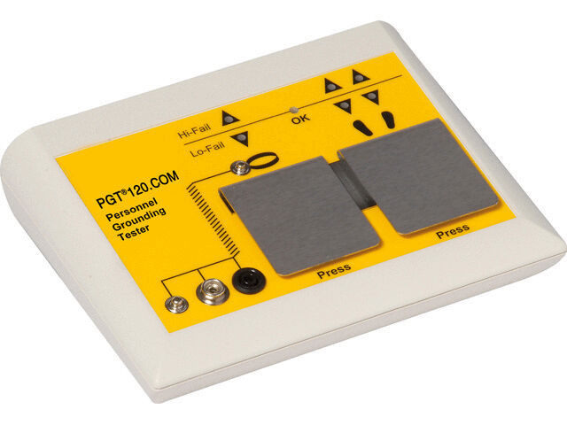 The image shows a yellow testing device with two large metal plates in the center. It has buttons and symbols, including "OK" and warning signs, for checking the grounding.