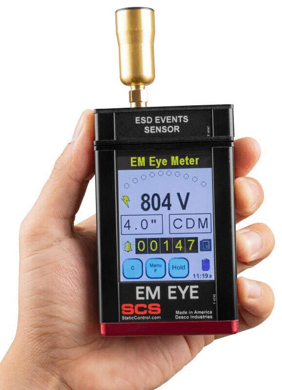 The image displays a handheld device for measuring electromagnetic fields. It features a display with values, buttons, and an antenna on top. The colors are red, black, and blue.