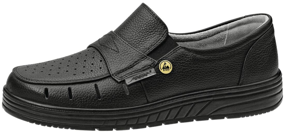 The image shows a black shoe with a flat, comfortable design. It has a durable upper, a wide Velcro strap, and ventilating holes. The sole is sturdy and textured.